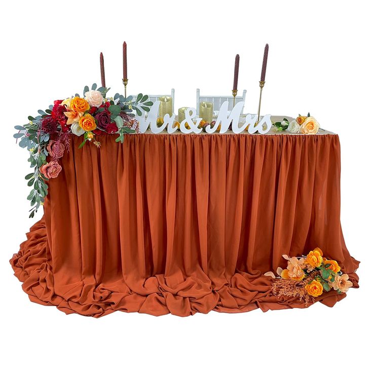 the table is covered with an orange drape and floral centerpieces, along with candles