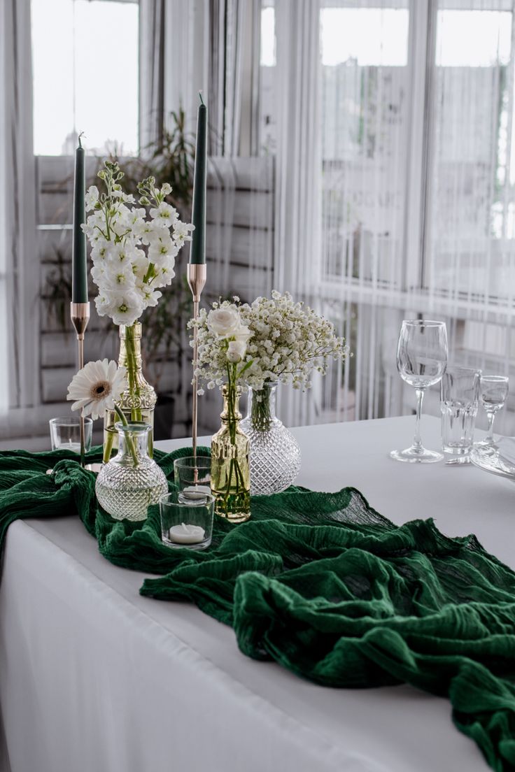 the table is set with white flowers and greenery in glass vases on it