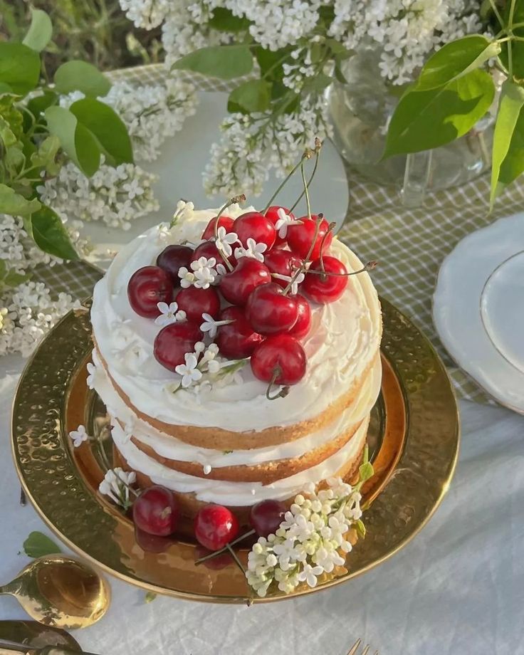 a cake with white frosting and fresh cherries on top is sitting on a gold plate