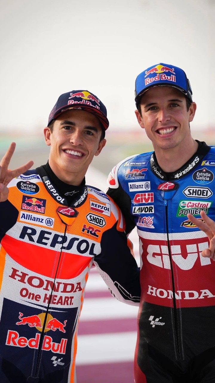 two men standing next to each other in front of a red bull race track with one holding up the peace sign