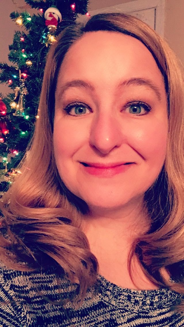 a woman smiling in front of a christmas tree