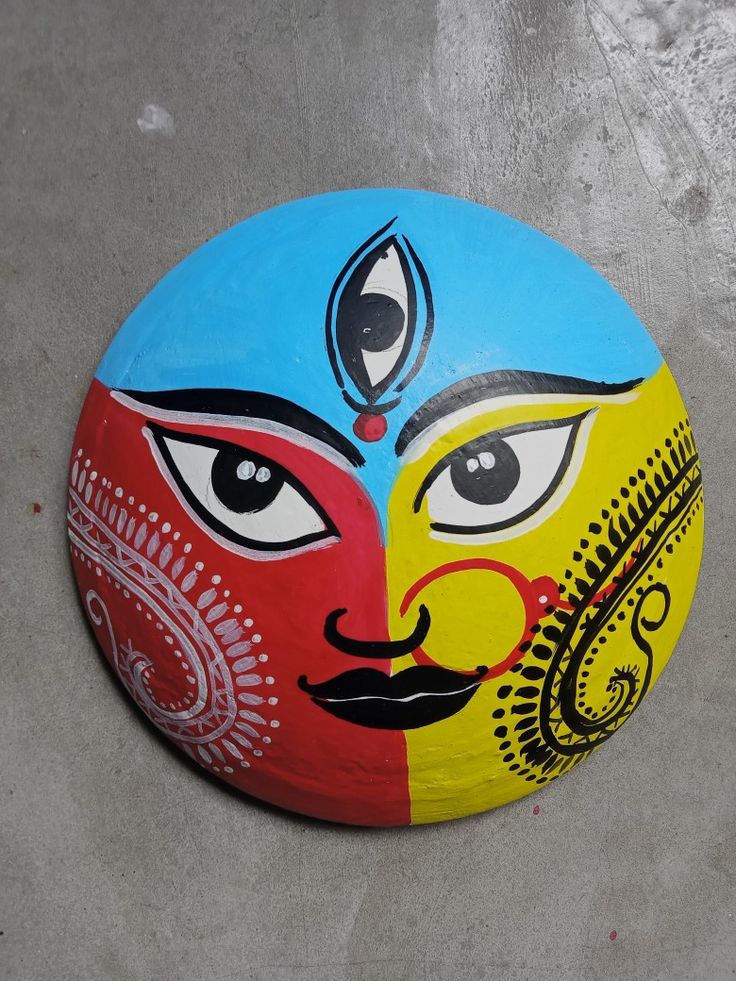 a painted rock with two faces on the front and one face on the back in different colors