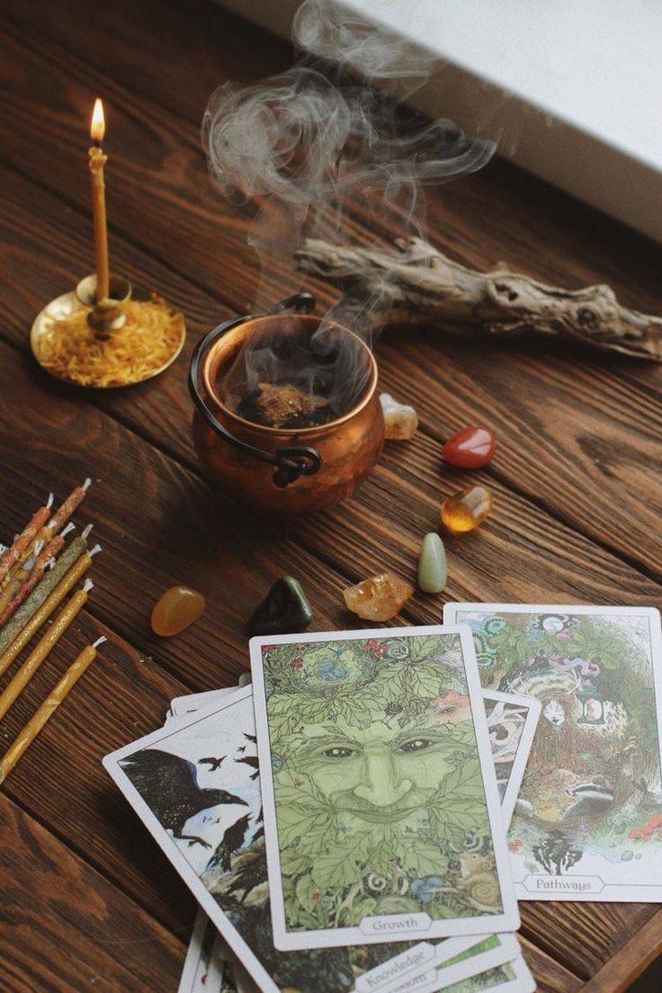 a wooden table topped with lots of cards next to a candle and some incense sticks