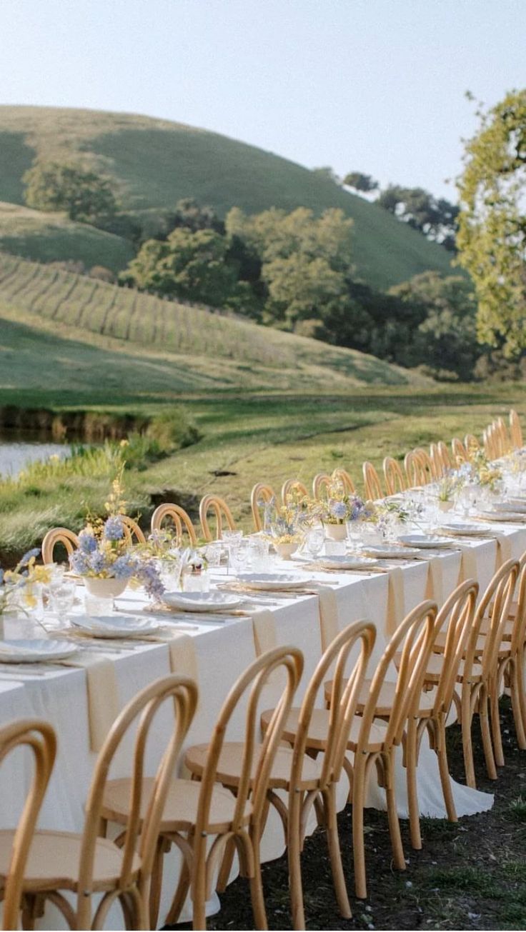 a long table is set up with white linens and place settings for an outdoor dinner