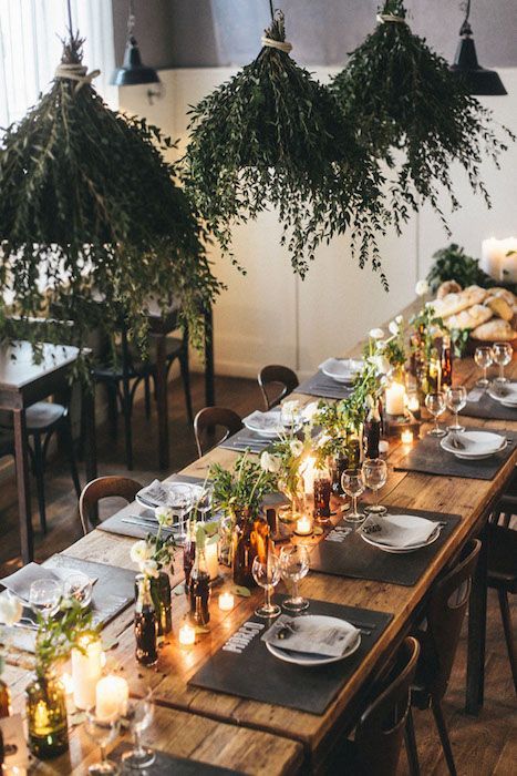 a long table with candles, plates and greenery hanging from it's ceiling