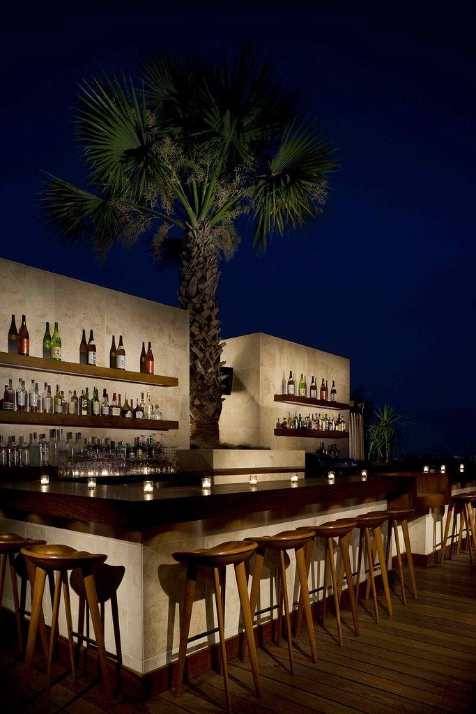 an outdoor bar with wooden stools and palm tree in the foreground at night