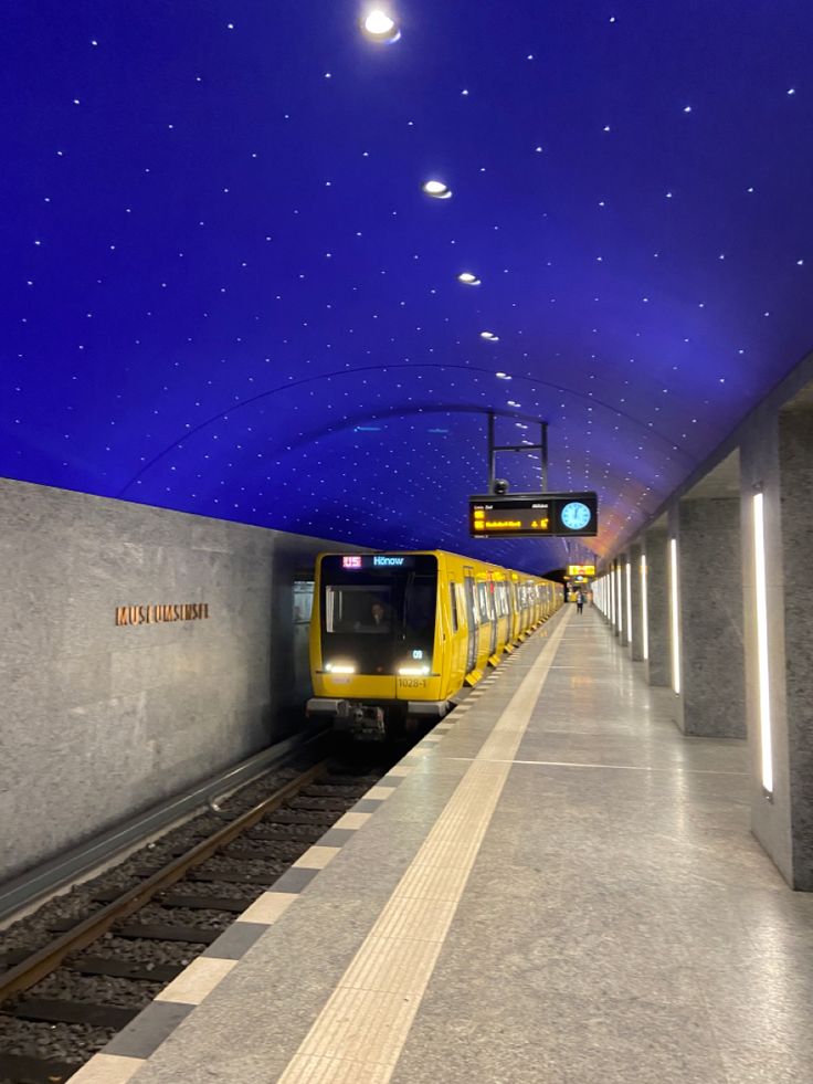 a yellow train pulling into a station under a blue sky with stars on the ceiling