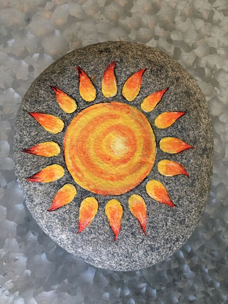 a painted rock sitting on top of a stone covered in gravel and rocks with leaves