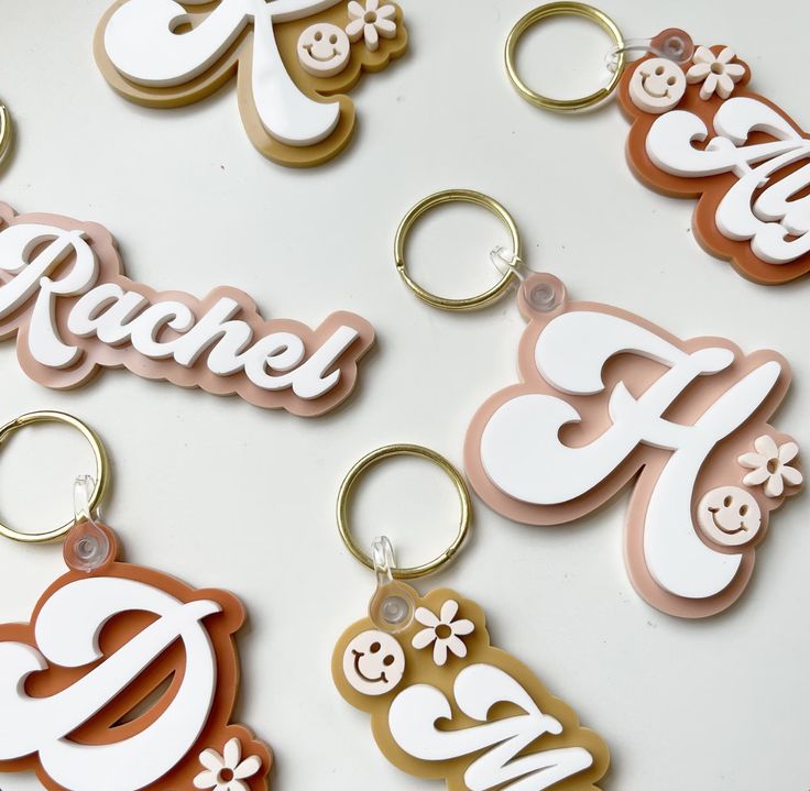 several keychains with different designs on them sitting on a white surface and one has the word rachel written in it