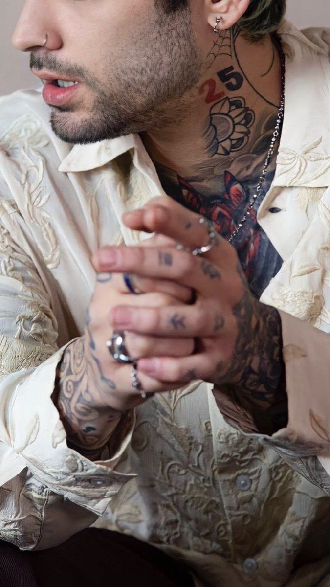 a man with tattoos on his arms and chest wearing a white shirt, looking off to the side