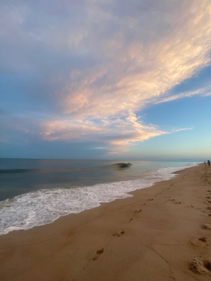 people are walking along the beach as the sun goes down and some waves come in