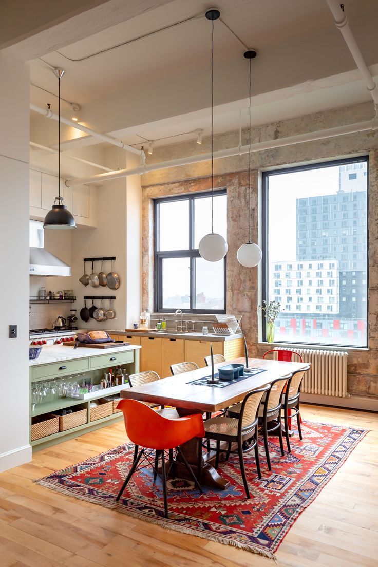 an open kitchen and dining room area with wooden floors, large windows, and colorful rug on the floor