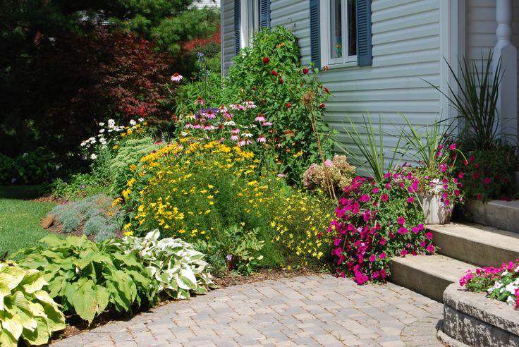 a house with flowers and plants in the front yard, next to steps that lead up to it