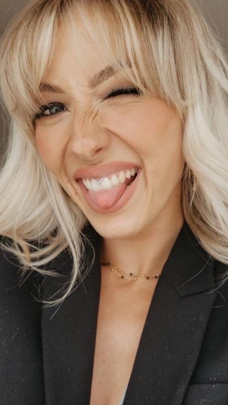 a woman with blonde hair smiling and wearing a black blazer over a white shirt