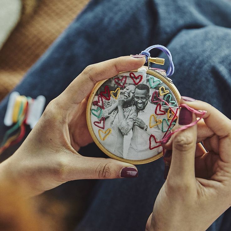 a woman is holding up a small embroidery hoop with an image of a man on it