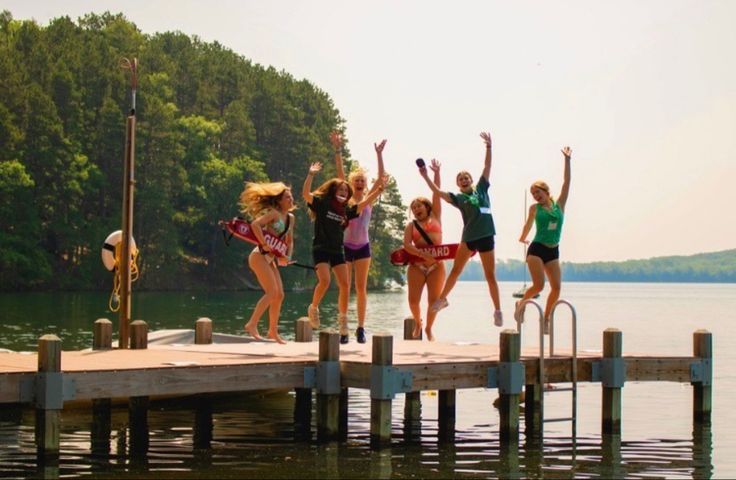 four girls jumping off a dock into the water with their arms up in the air