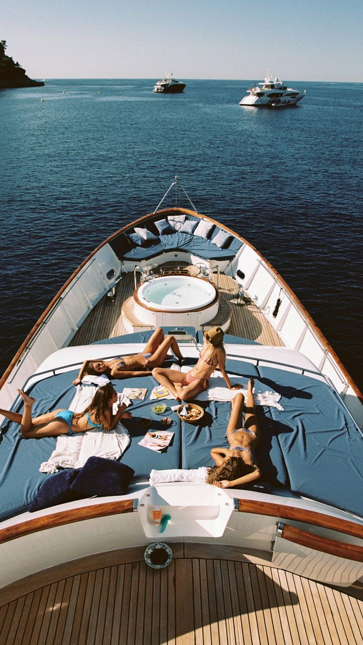 people lounging on the back of a boat in the water with boats behind them