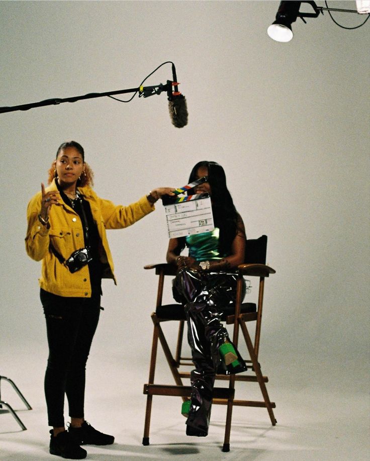 two women sitting in chairs with microphones behind them and one woman holding a sign