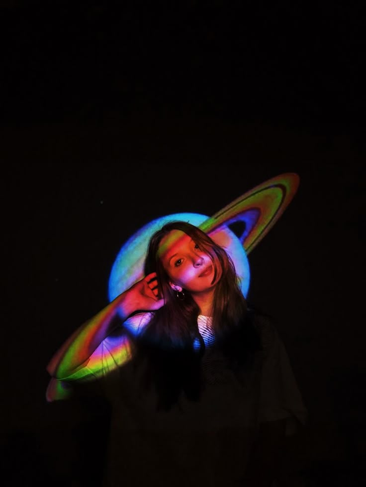 a woman wearing a colorful hat with her hands behind her head in the dark while holding a frisbee