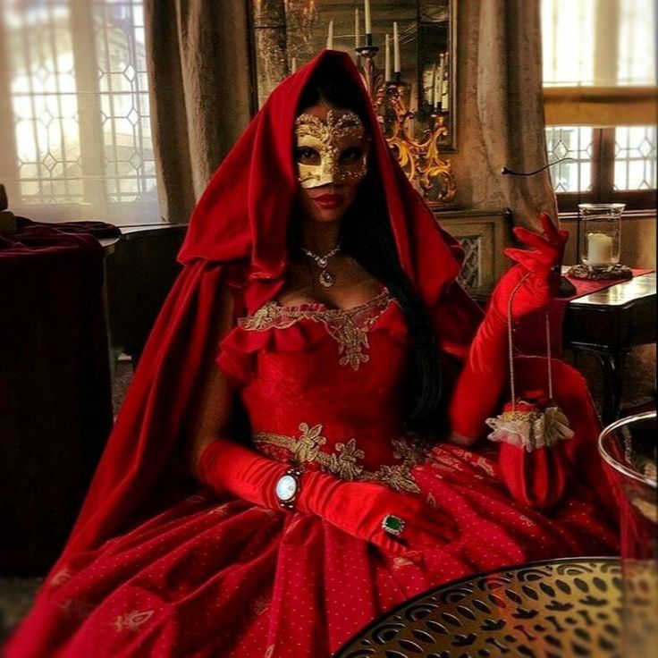 a woman in a red dress and mask sitting on a table