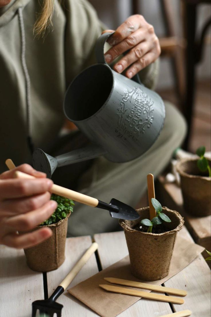 a woman is holding a potted plant and watering it with a garden tool while sitting on a table