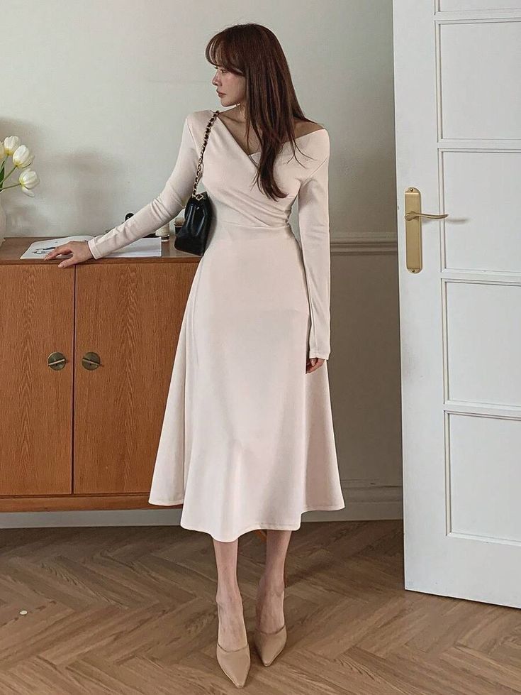 a woman standing in front of a wooden cabinet wearing a white dress with long sleeves