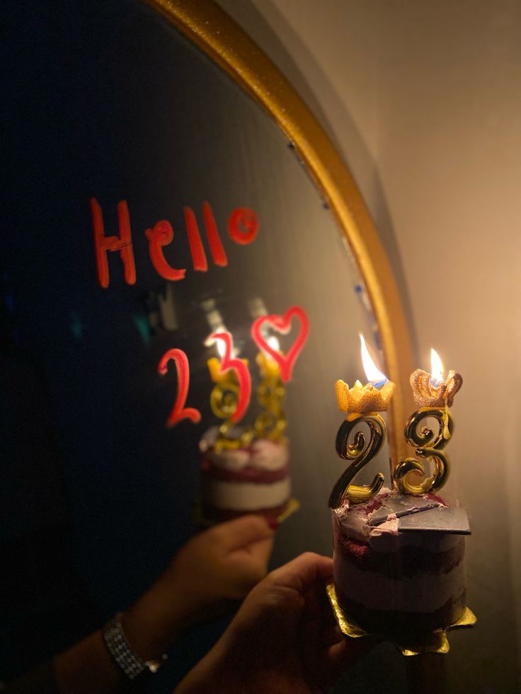 someone is holding a birthday cake with candles in front of the mirror that says hello 25