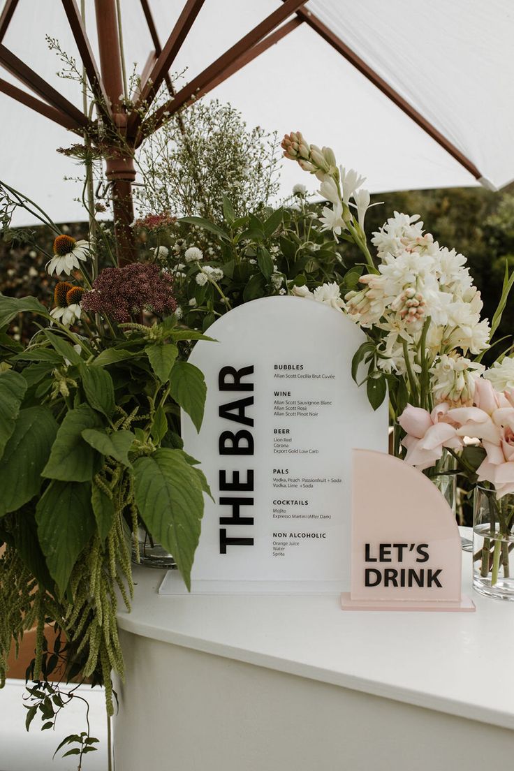 the bar sign is surrounded by flowers and greenery in glass vases on a white counter