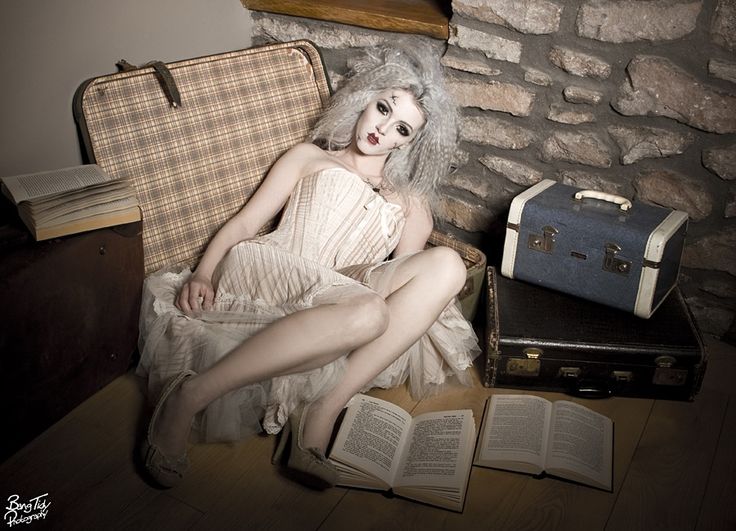 a creepy doll sitting on top of a chair next to an open book and suitcase