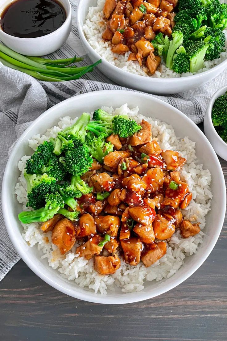 two white bowls filled with chicken and broccoli on top of rice next to sauce