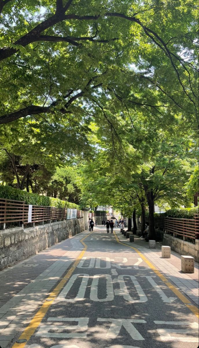 an empty street with trees lining the sides and people walking on the sidewalk in the distance