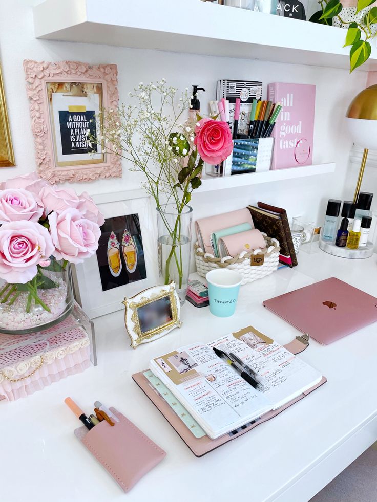 a white desk topped with lots of pink flowers and writing supplies on top of it