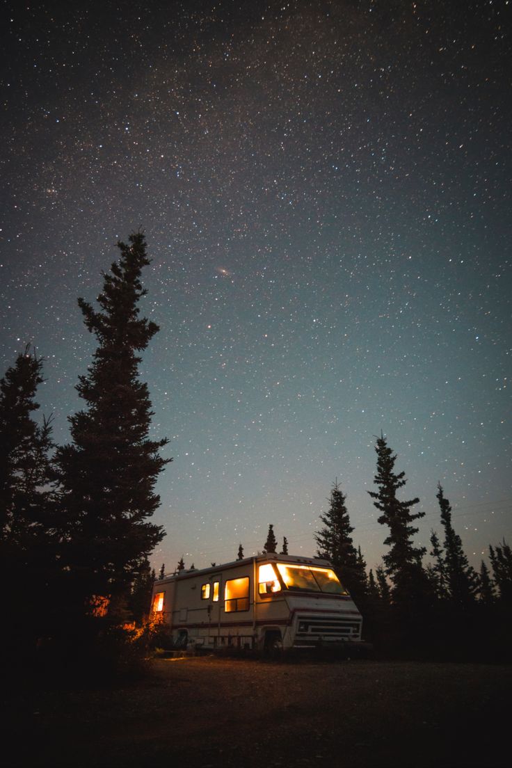 the night sky is filled with stars above a small camper trailer parked in front of some trees