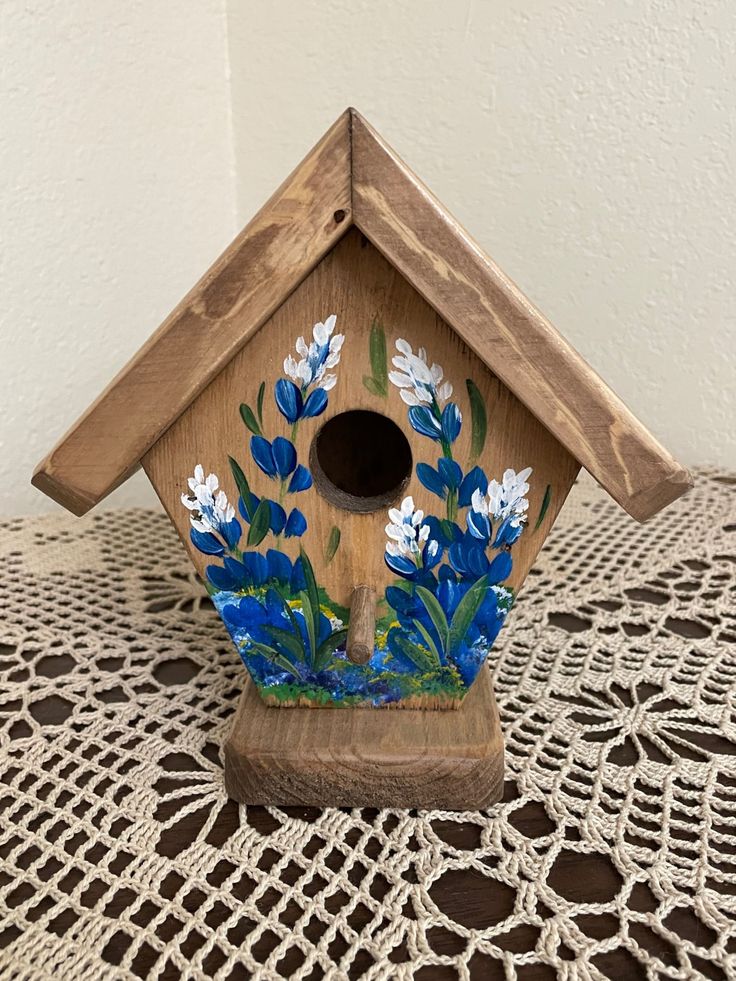 a birdhouse with blue flowers painted on it's side sitting on a doily