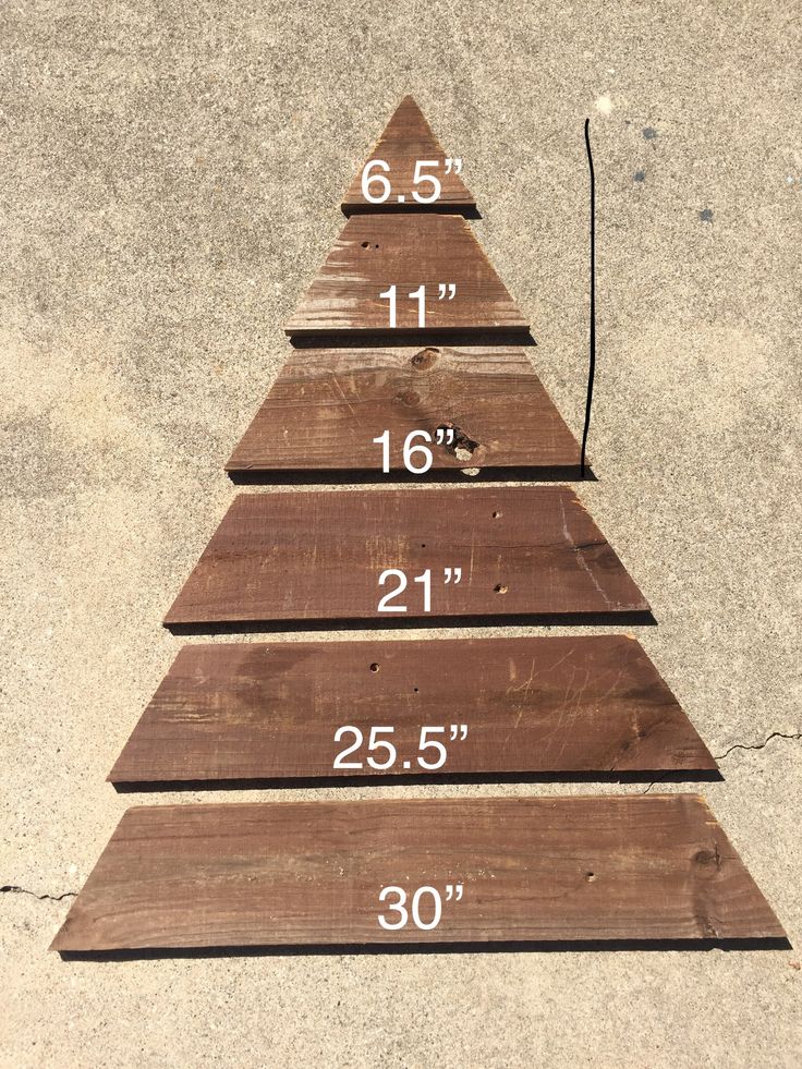 a wooden christmas tree sitting on top of a cement floor next to a measuring ruler