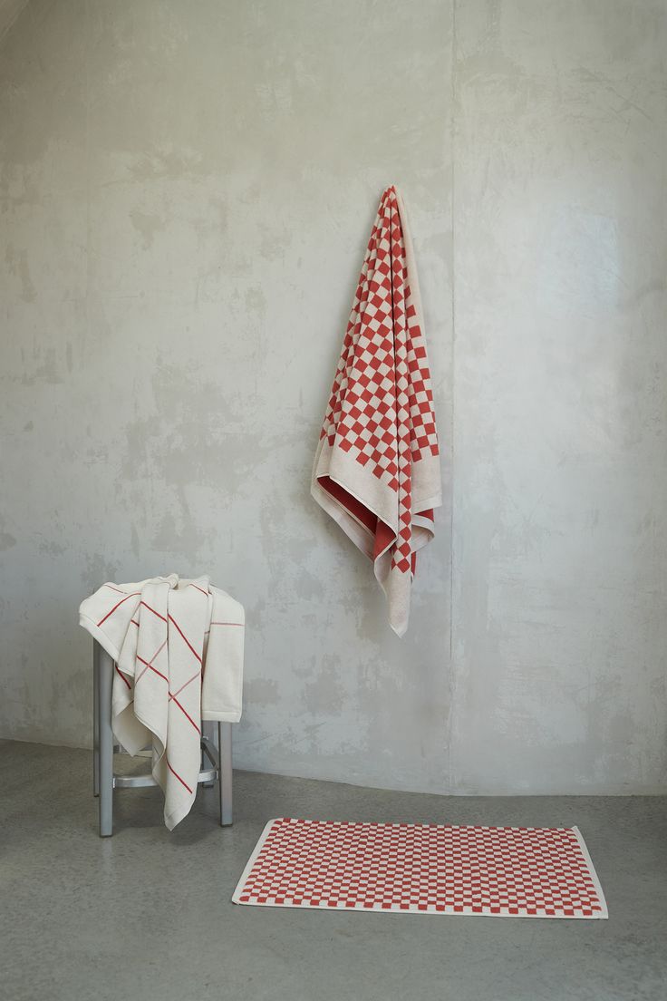 a red and white towel hanging on the wall next to a stool with two towels