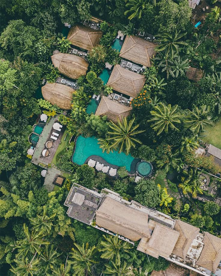 an aerial view of a resort surrounded by trees and grass covered houses with thatched roofs