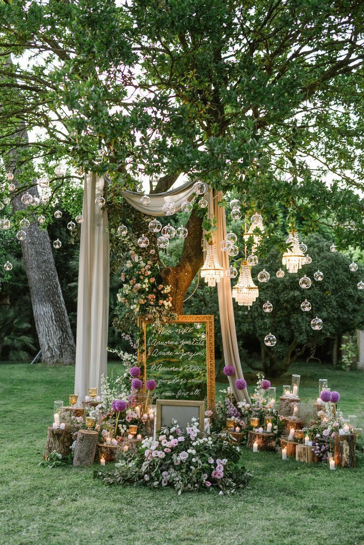 an outdoor ceremony setup with candles, flowers and greenery on the grass under a tree