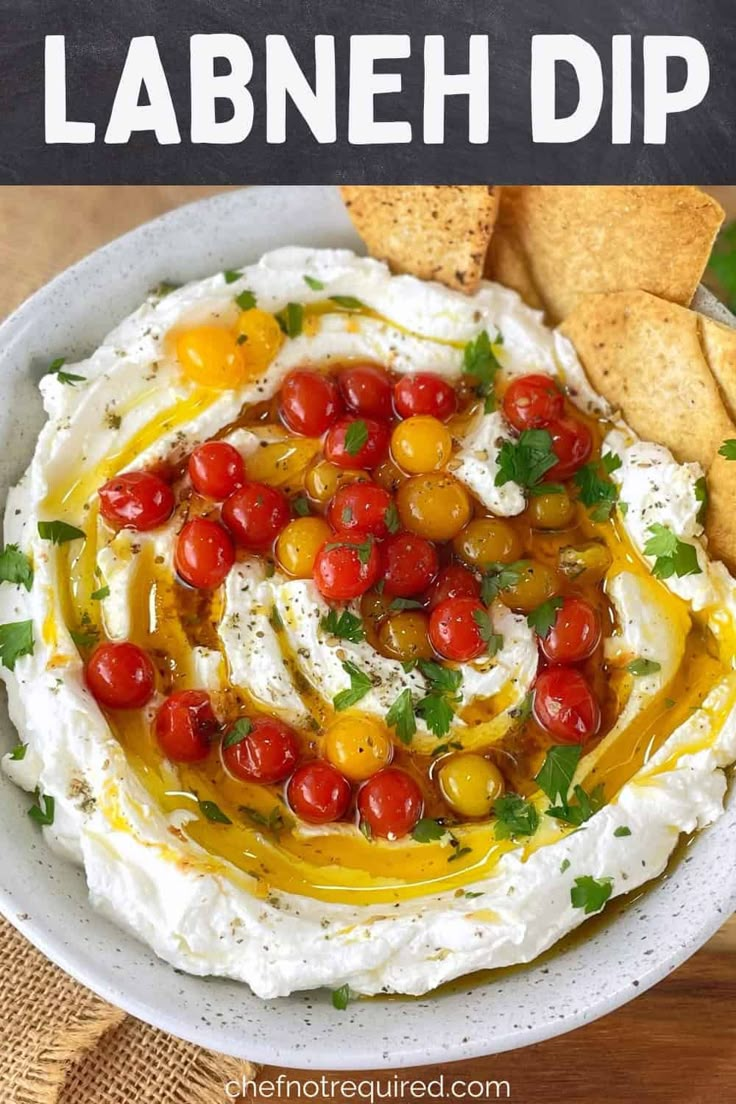 a white bowl filled with hummus, tomatoes and olives next to crackers