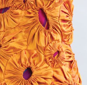 an orange pillow with purple ruffles on the front and back sides, sitting against a white background