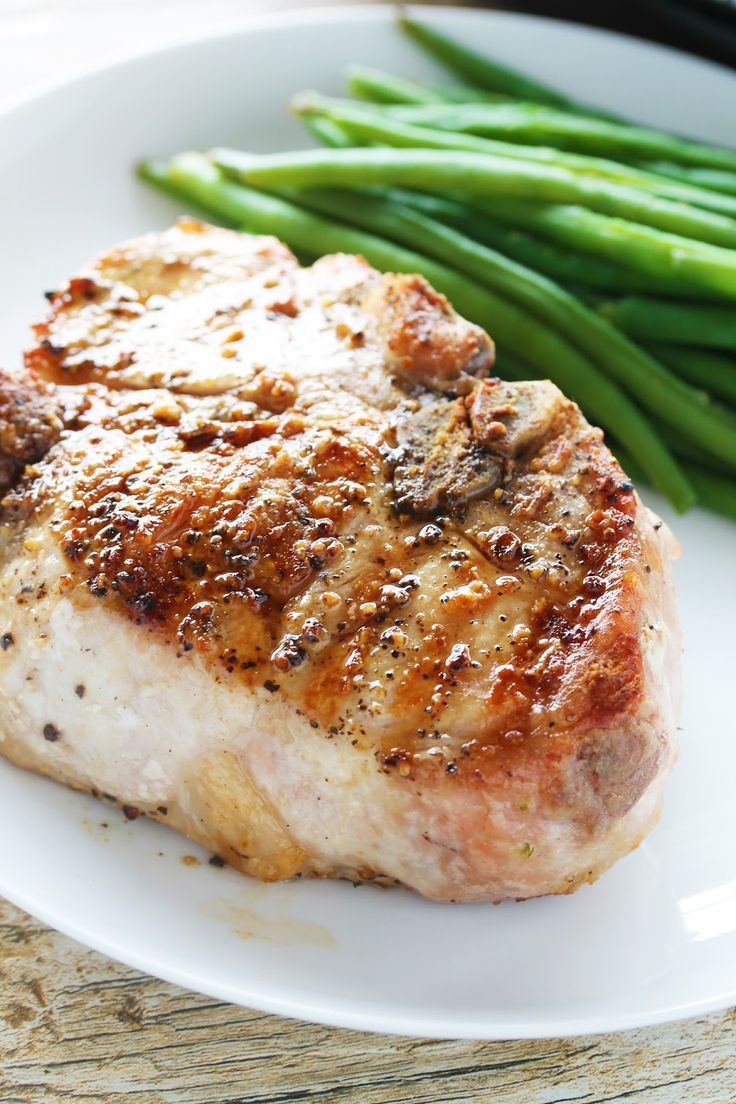 a piece of meat on a plate with green beans and asparagus next to it