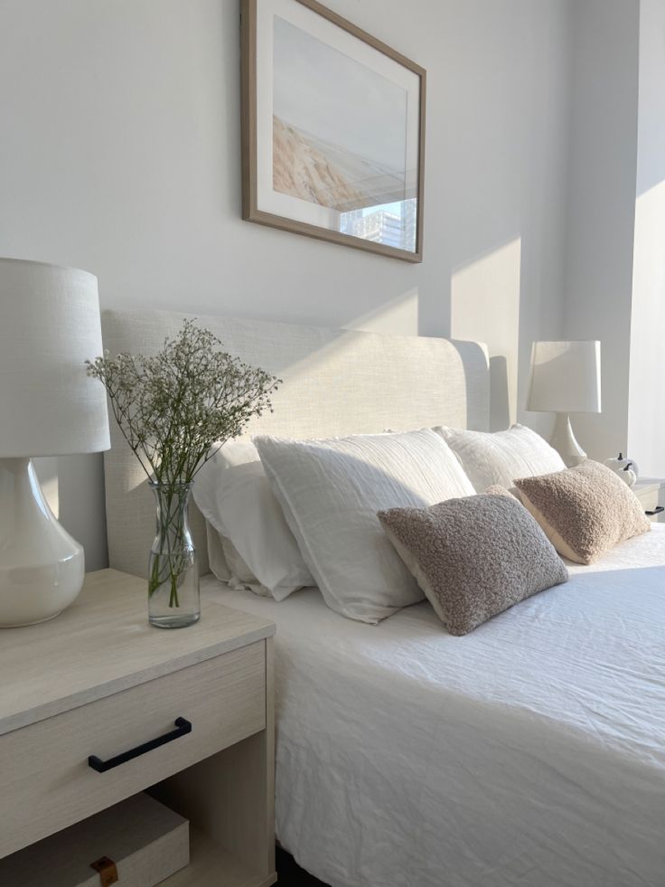 a bed with white sheets and pillows next to a vase filled with flowers on top of it