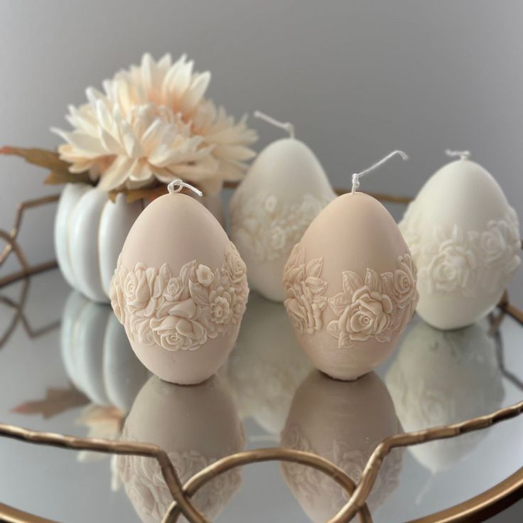 three eggs sitting on top of a glass table next to a white and gold flower