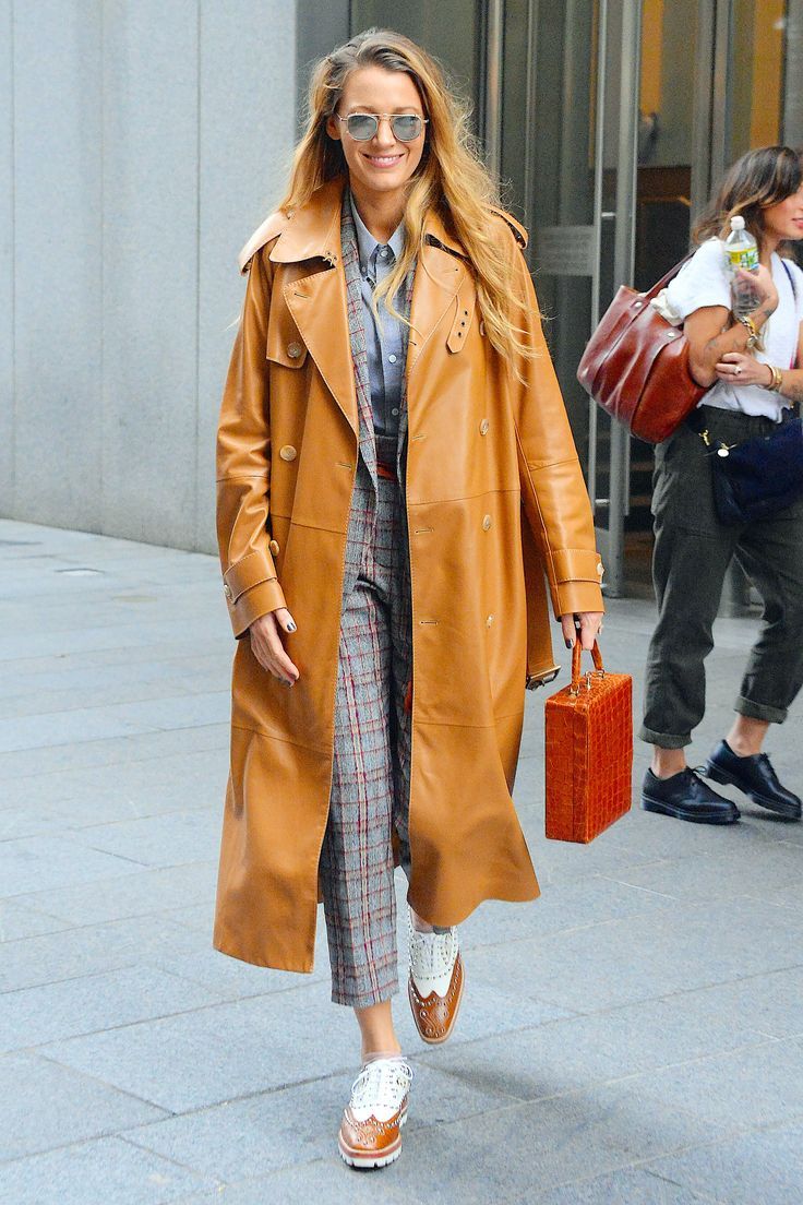 a woman walking down the street in a trench coat and plaid pants with white sneakers