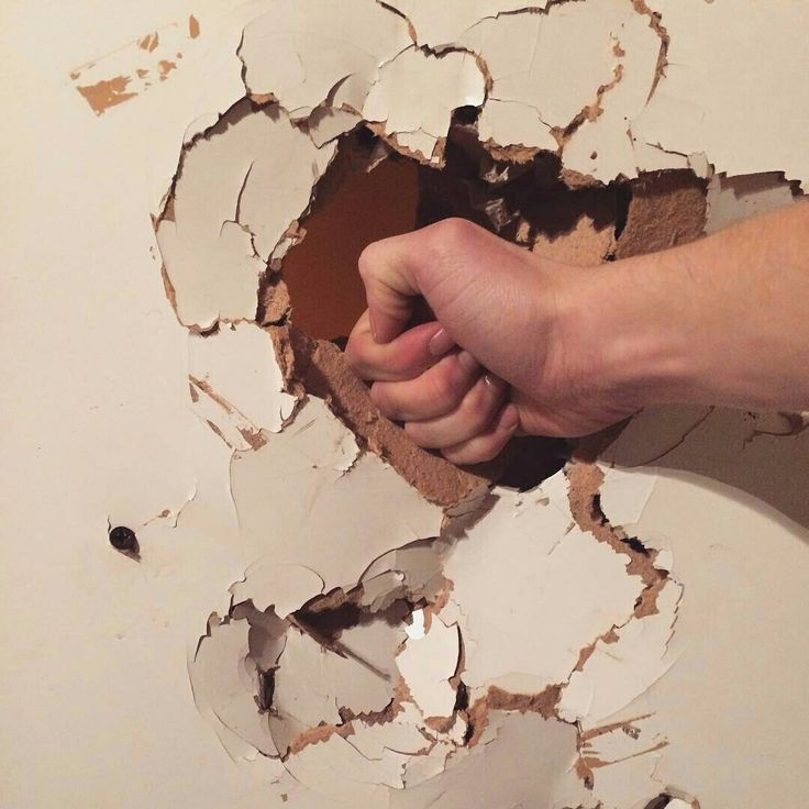 a person's hand breaking through a hole in a wall with paint on it