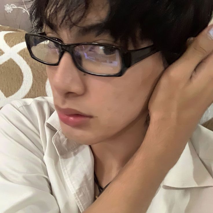 a young man wearing glasses sitting on top of a couch