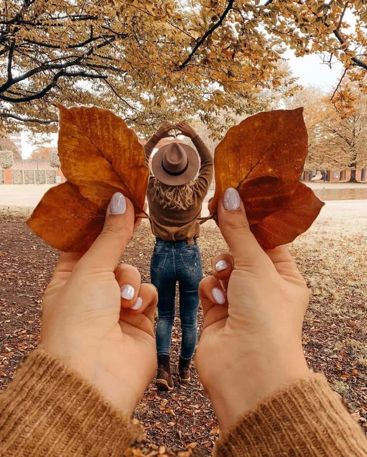 two hands holding up leaves in front of a woman's face with her hat on