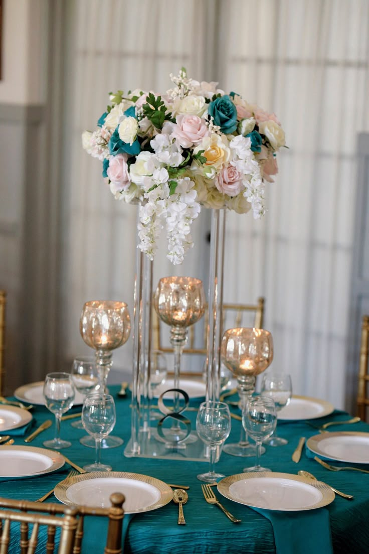 a table set with plates, silverware and flowers in tall vases on it