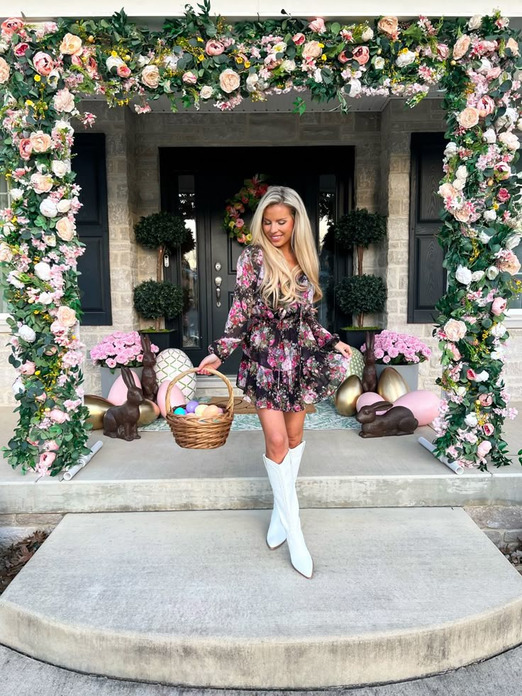 a woman standing in front of a flower covered entrance with easter decorations and flowers around her