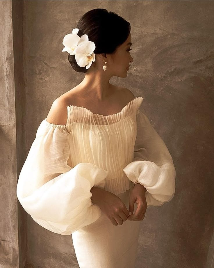 a woman in a white dress with flowers in her hair standing next to a wall